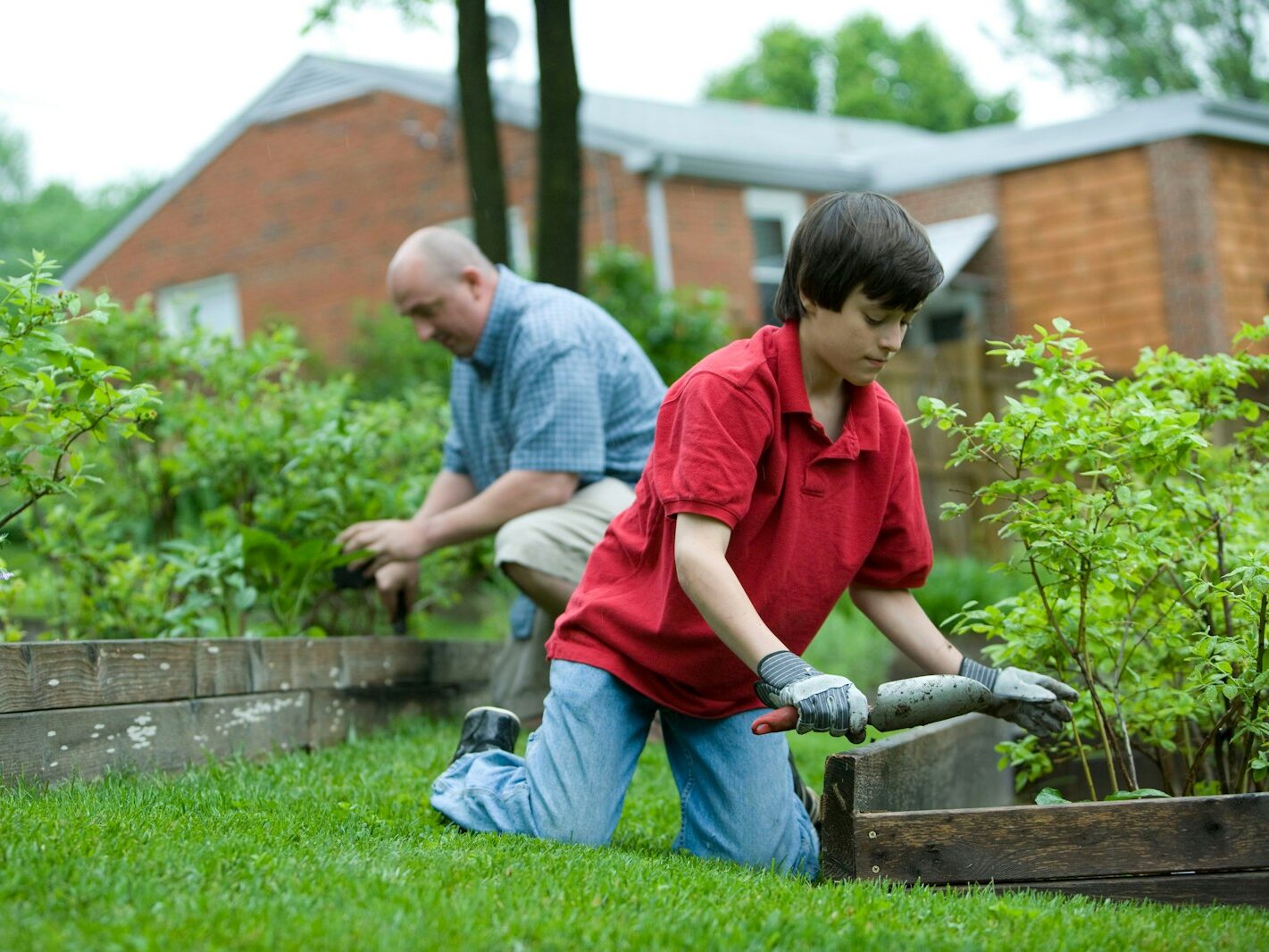 man in red polo shirt and blue denim jeans sitting on brown wooden bench during daytime