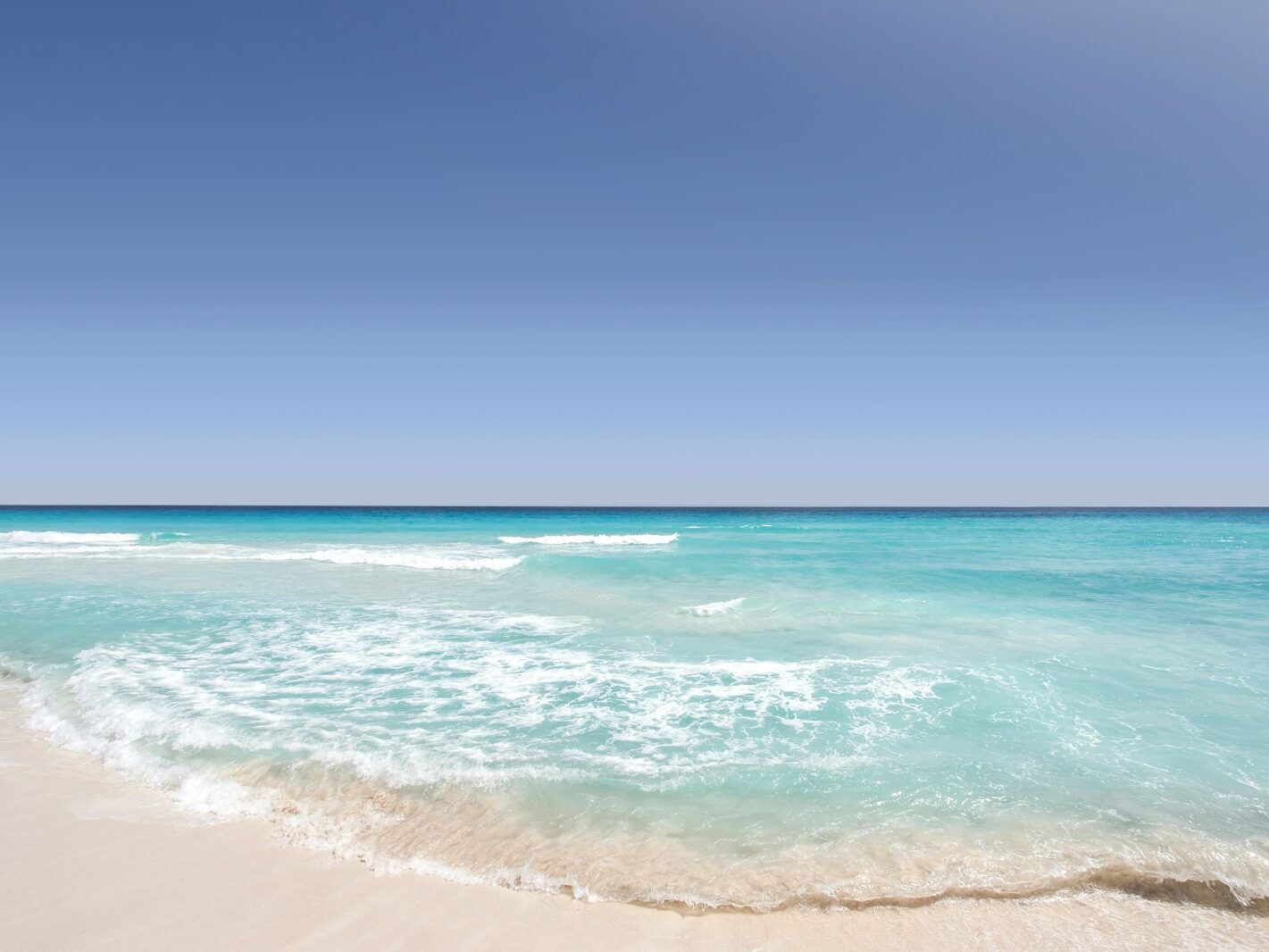 Clear blue ocean washing on the sandy shore on a clear day in Cancún
