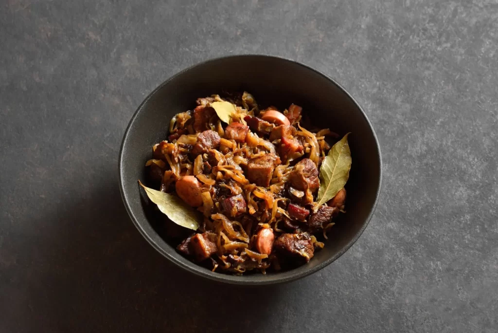 Tradiční polský Bigos v misce na tmavém kamenném pozadí. Dušené zelí s kysaným zelím, houbami, uzeným masem a kořením. Pohled zblízka